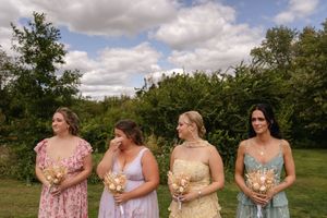 Bridesmaids in pastel dresses hold bouquets while standing in a row outdoors.