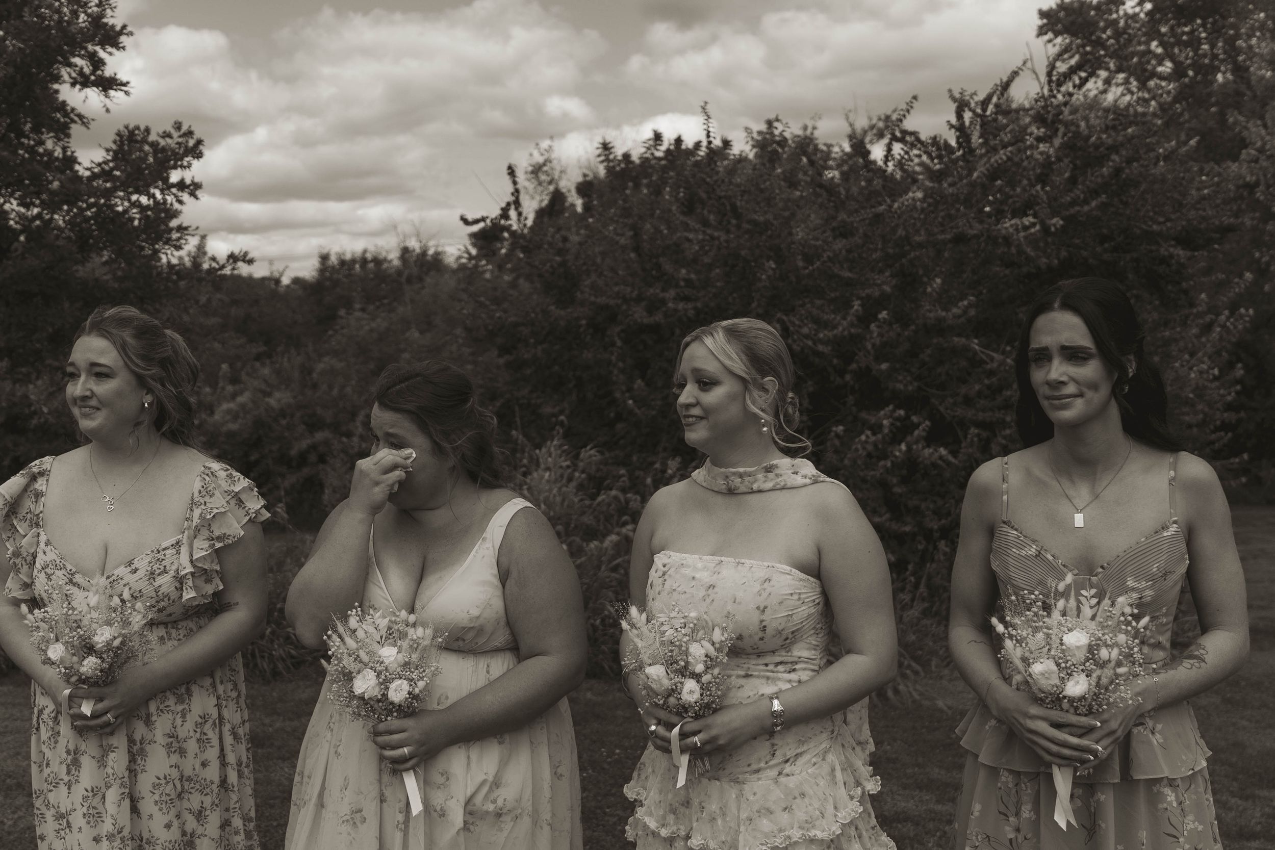 Bridesmaids in pastel dresses pose together holding bouquets during outdoor wedding photography.