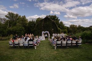 Wide angle shot of wedding guests seated in white chairs on a sunny hillside.