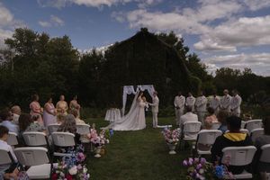 Outdoor wedding ceremony setup with white chairs and guests under blue skies.