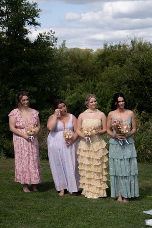 Wedding party in pastel dresses holding bouquets while standing on grass.