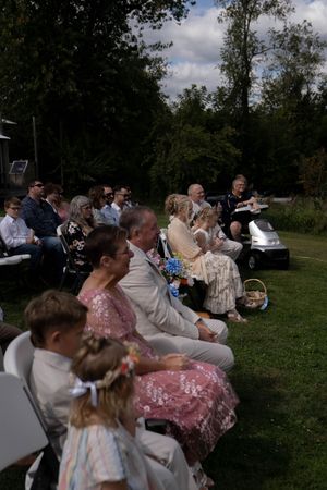Wedding guests seated in white chairs on a grassy hillside during an outdoor ceremony.
