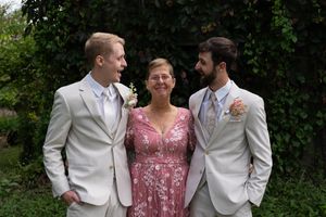 Wedding party members in white suits and pink dress pose in garden setting.