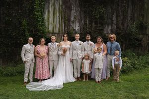 Wedding party members in light colored attire pose together on a grassy lawn for formal group photos.