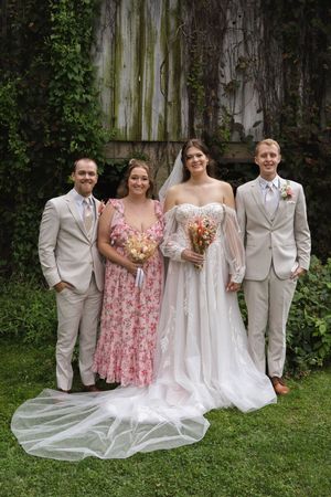 Wedding party members in white gowns and suits pose with pink floral accents.