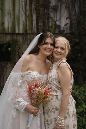 Close-up wedding portraits showcase delicate lace details and coral-colored bouquet against wooden backdrop.