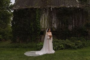 Elegant wedding dress with flowing train displayed against rustic stone wall backdrop.
