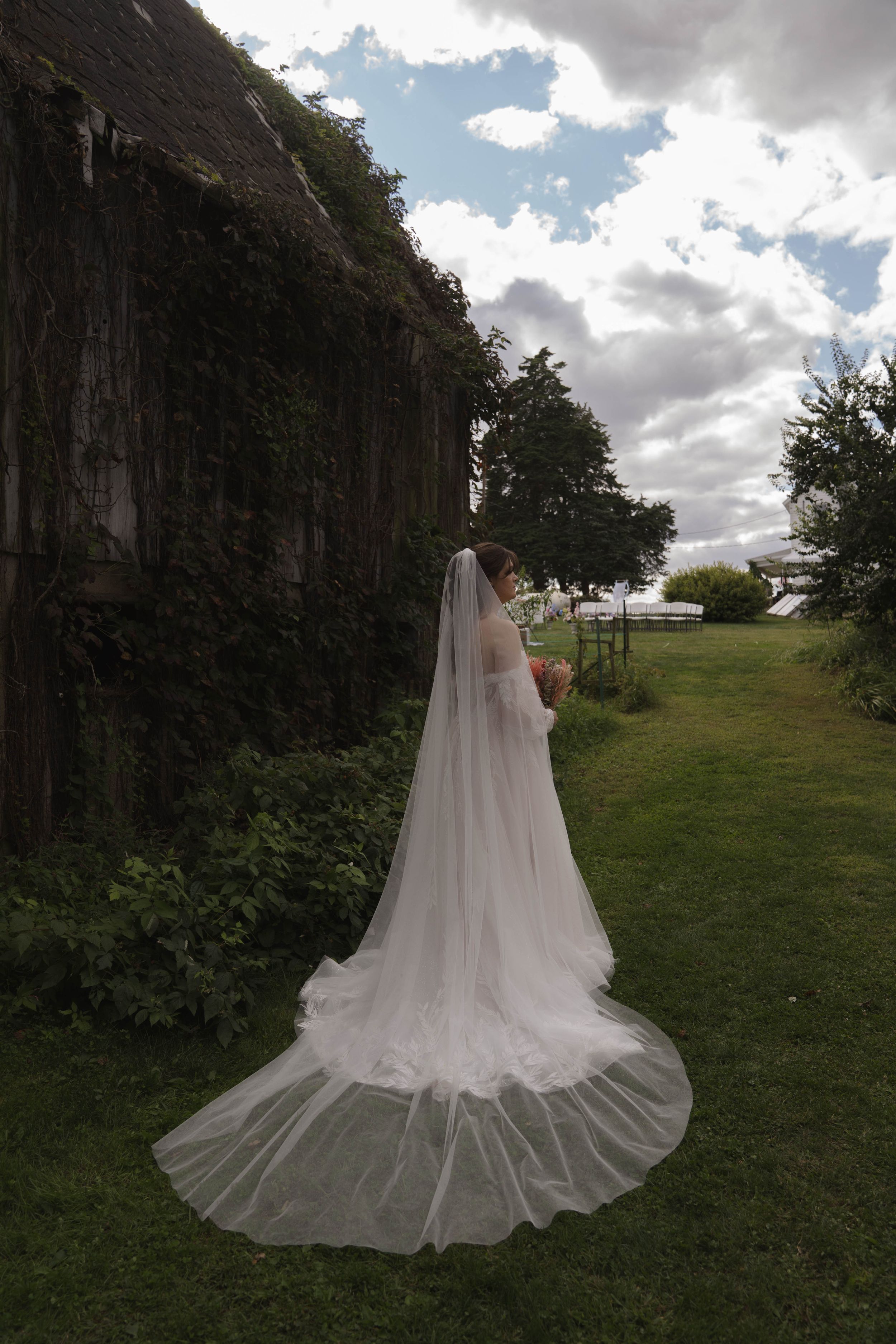 Dramatic bridal portrait showcasing long cathedral veil against cloudy sky.
