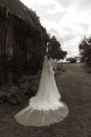 Black and white photo series of wedding dress with dramatic train on grassy hillside.