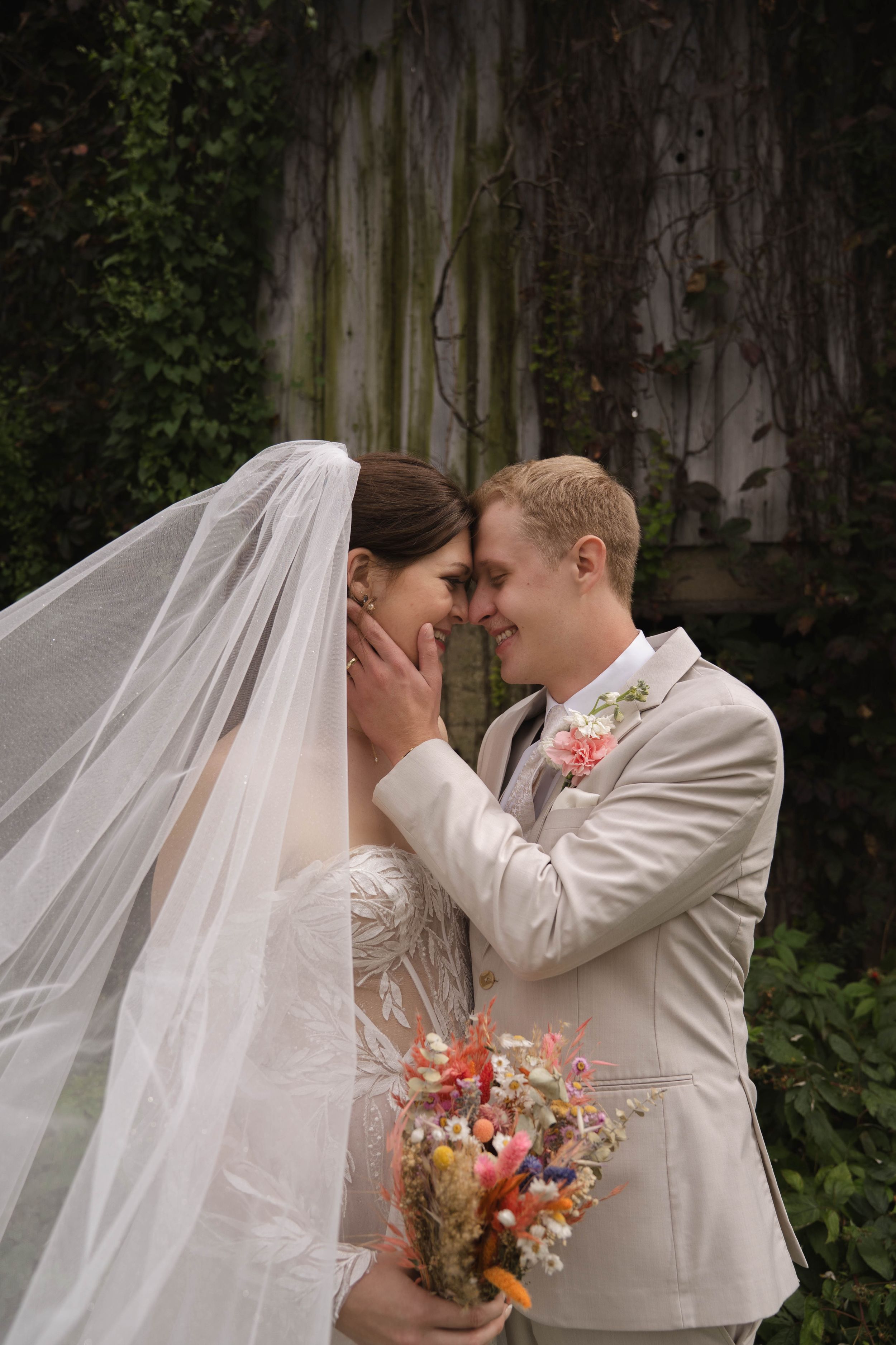Intimate wedding moment captured with colorful bouquet against rustic wooden backdrop.