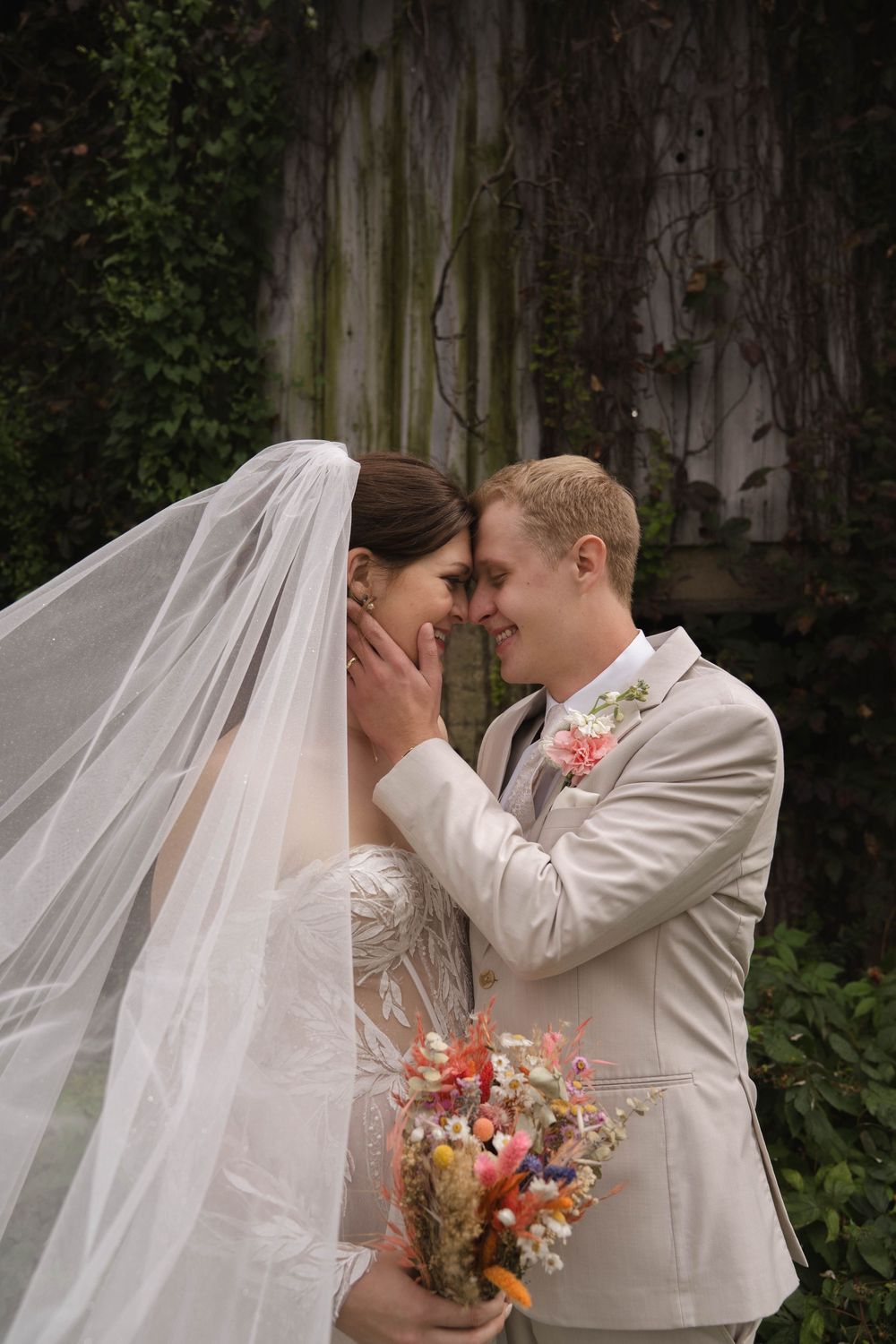 Intimate wedding moment captured with colorful bouquet against rustic wooden backdrop.