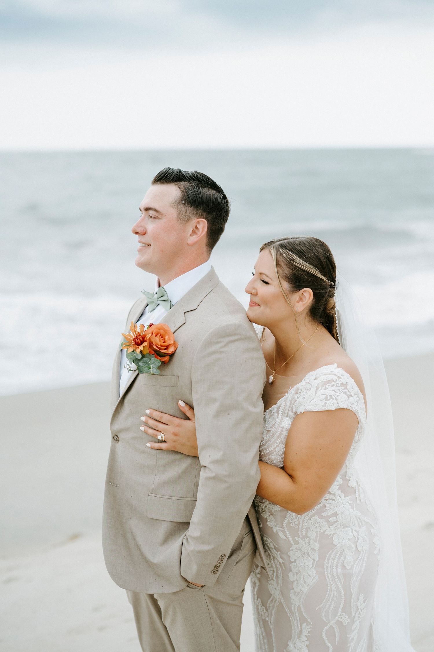 A couple shares intimate moments at their beachfront wedding ceremony dressed in white and beige.