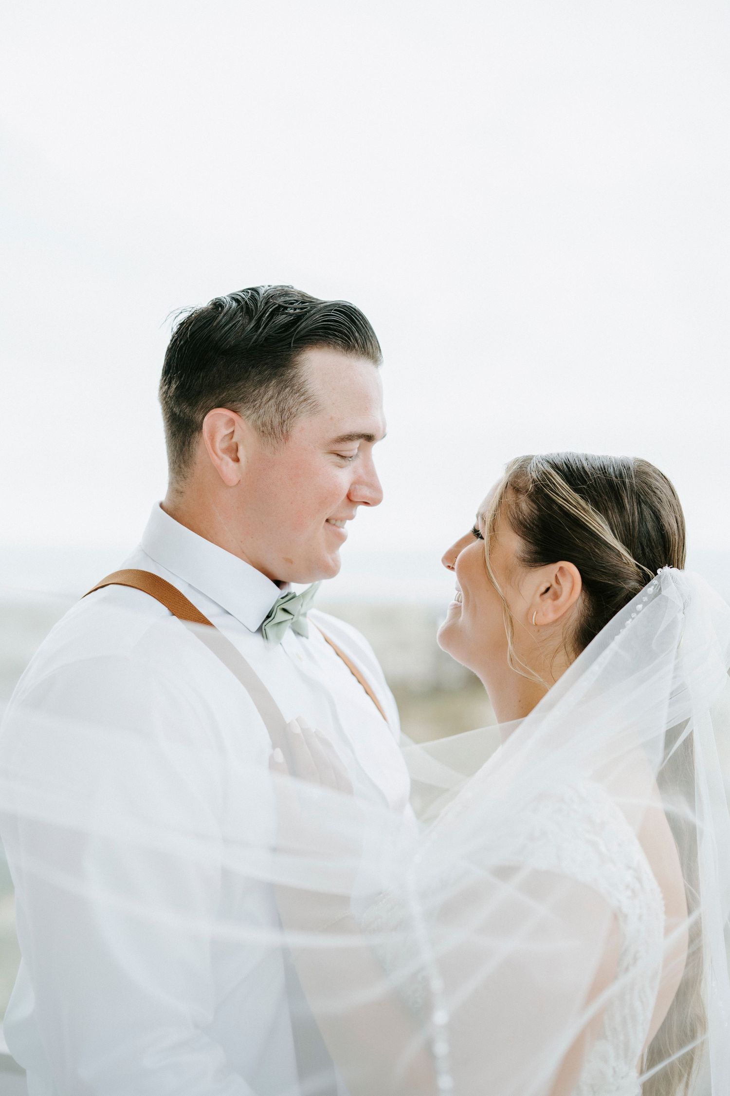 Romantic beach wedding portrait with flowing white veil catching the breeze.