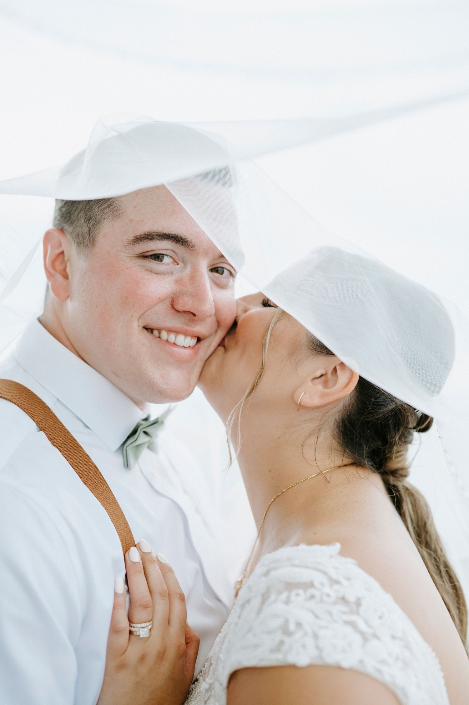 Intimate wedding couple moment captured in bright white lighting with leather suspenders and lace details.