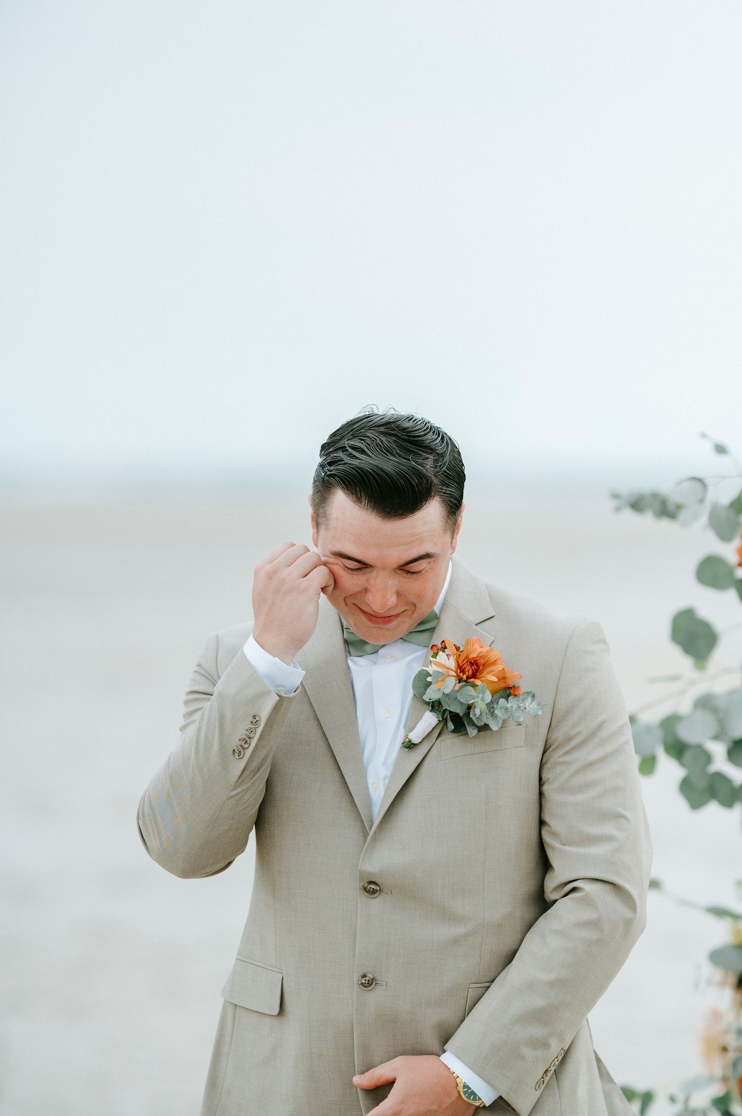 Emotional moment captured as groom wipes away tears during beach wedding ceremony.