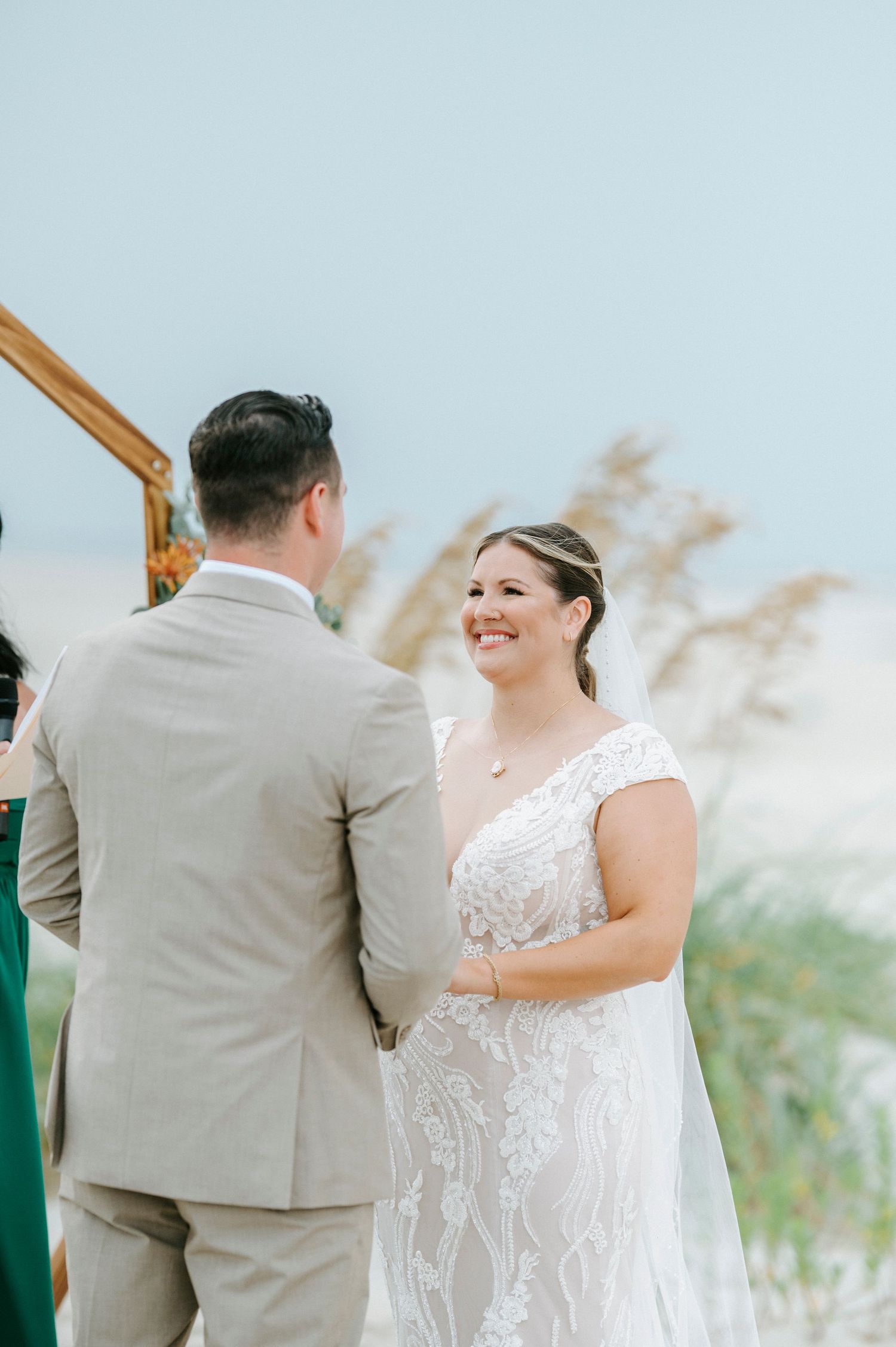 A joyful wedding ceremony moment under a wooden hexagon arch decorated with flowers on the beach.
