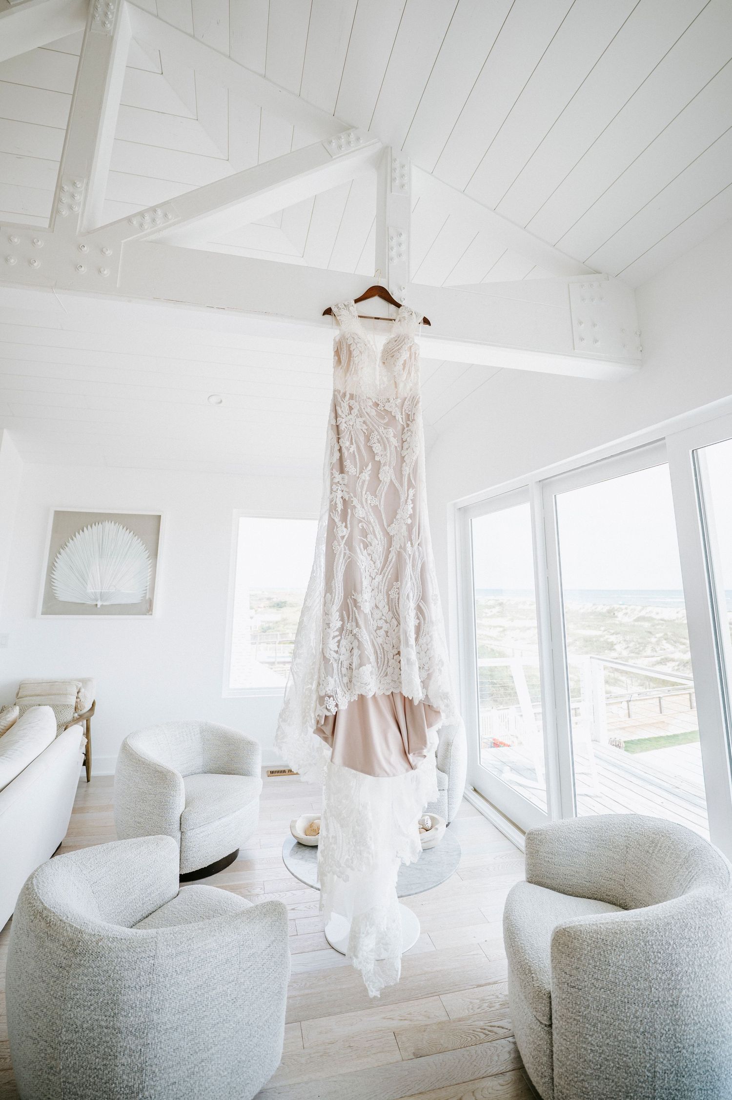 White interior room with plush chairs and lace wedding dress hanging against shiplap ceiling and walls.