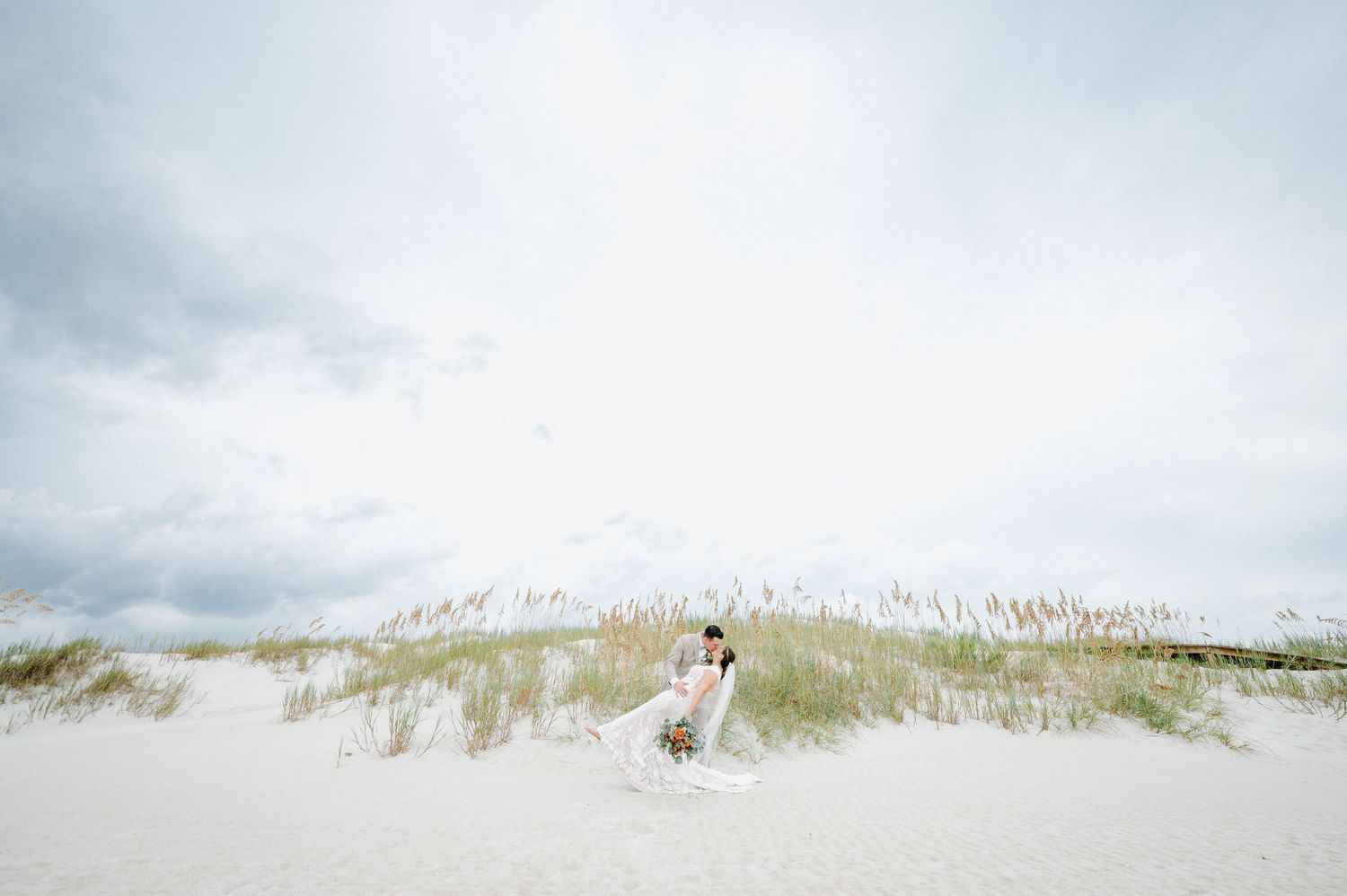 Panoramic view of beach grass and dunes under cloudy coastal skies.