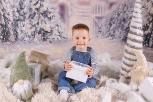 A child sits in a winter wonderland photo session with white snow-covered trees and sparkly holiday decorations.