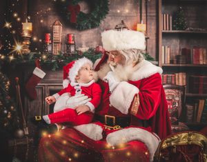 Traditional Christmas scene of Santa Claus sitting by a fireplace with wrapped presents and twinkling holiday lights.