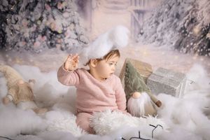 Baby in pink outfit lies amongst cotton-like clouds and twinkling lights in dreamy winter photo shoot setting.