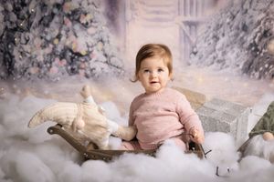 Children in cozy winter outfits pose amongst snowy winter wonderland decorations for a festive holiday photoshoot.