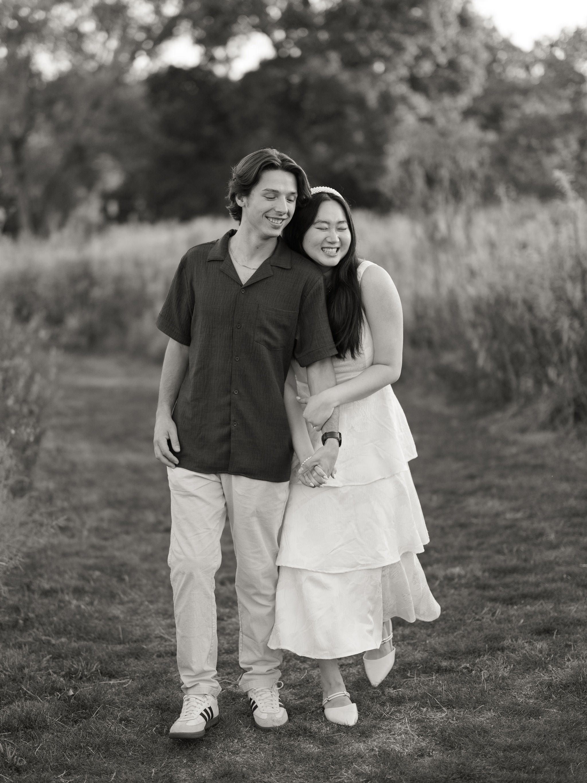 A happy couple shares joyful laughter and embraces while walking together outdoors in a black and white photo series.