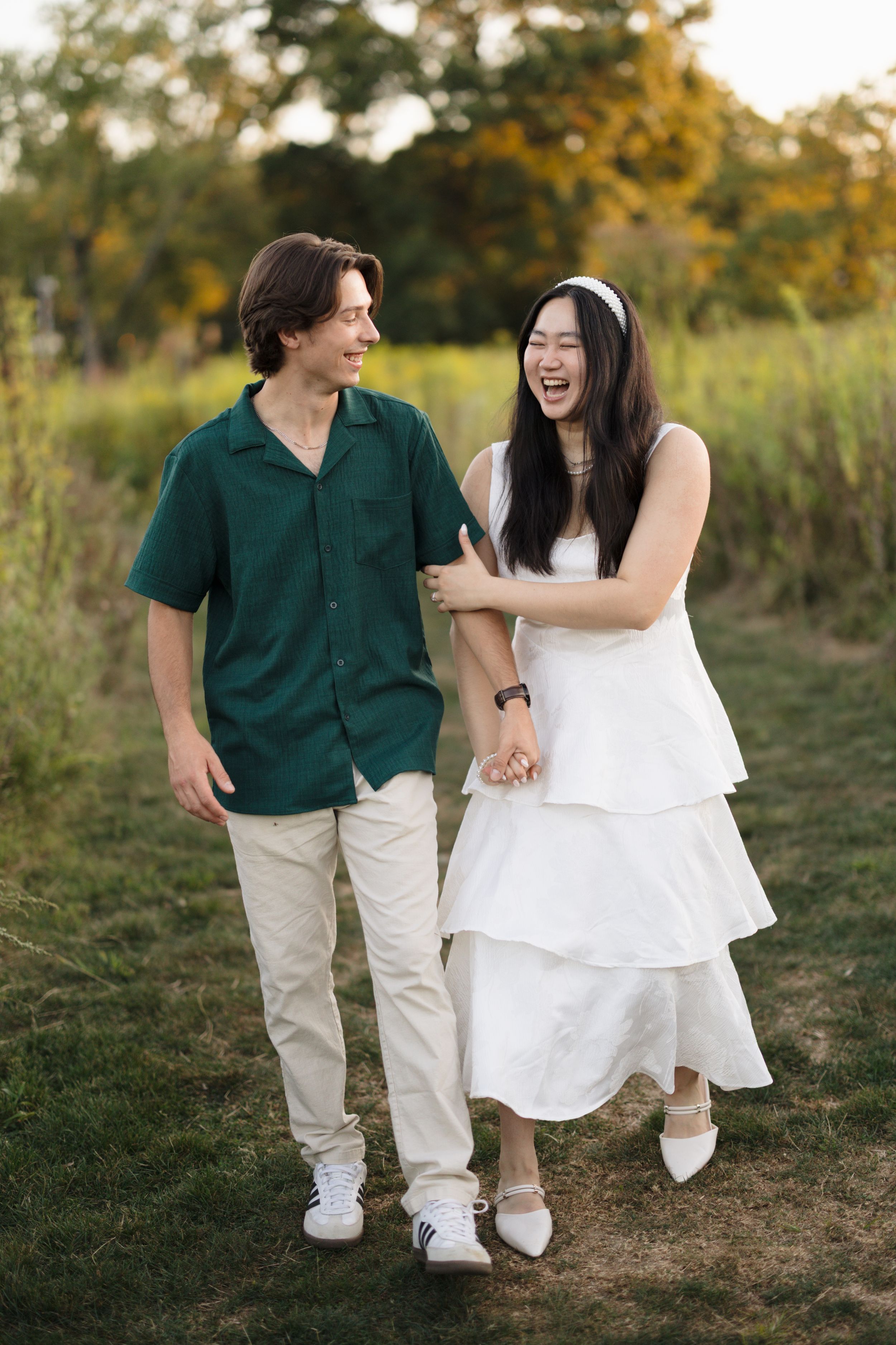 Couple in contrasting green and white outfits laughing together during outdoor photo session.
