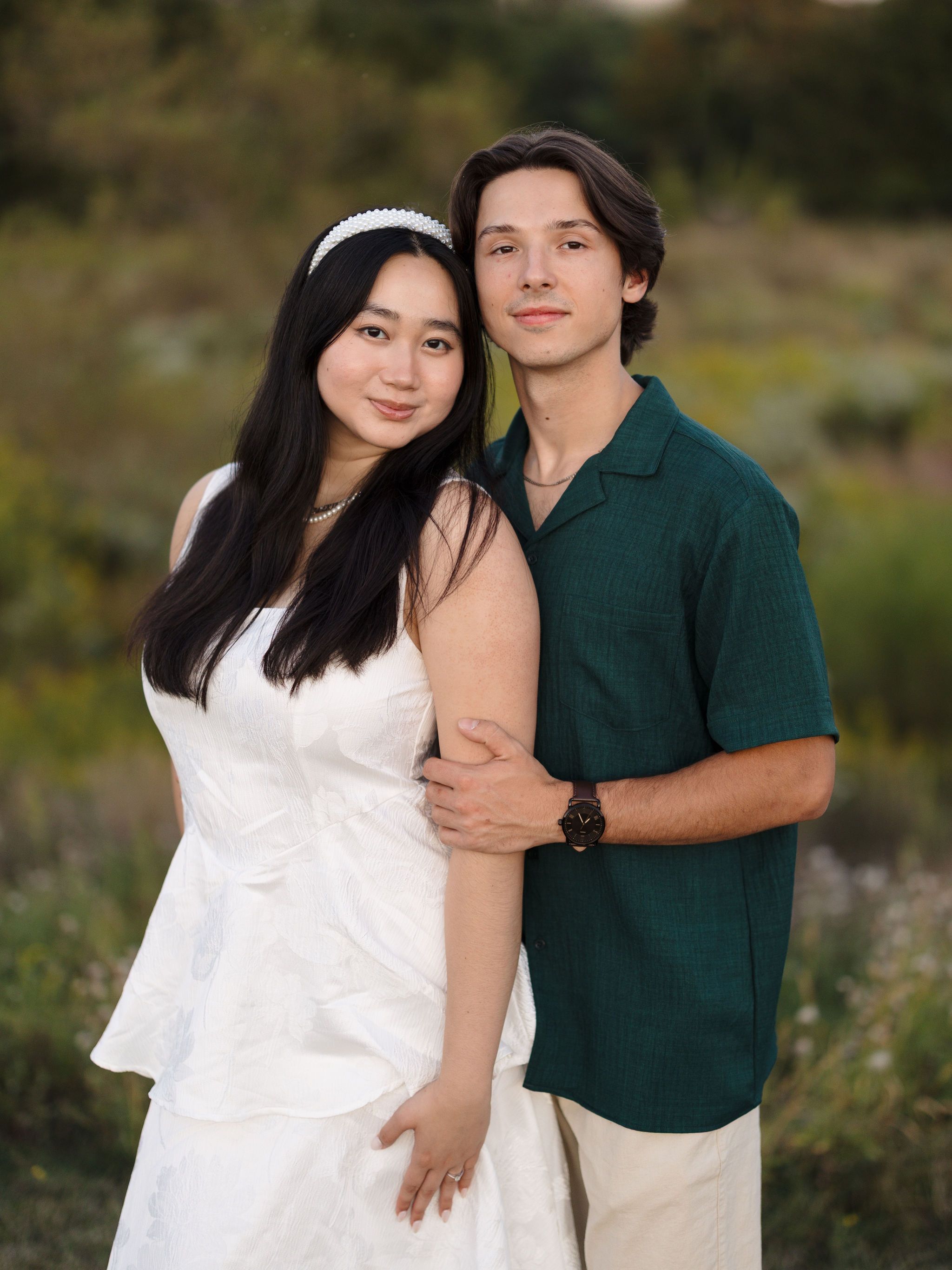 A couple embraces in casual attire during a sunset photoshoot in a rural outdoor setting.