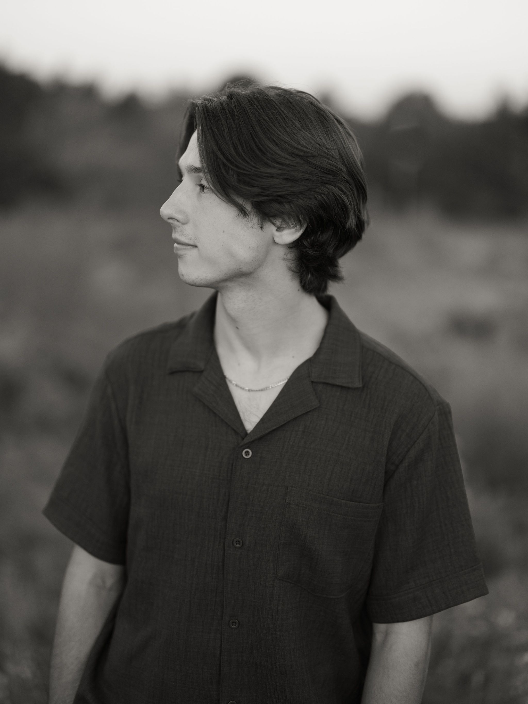 Black and white portrait photograph of a person in profile view wearing a short-sleeved button-up shirt against a blurred background.