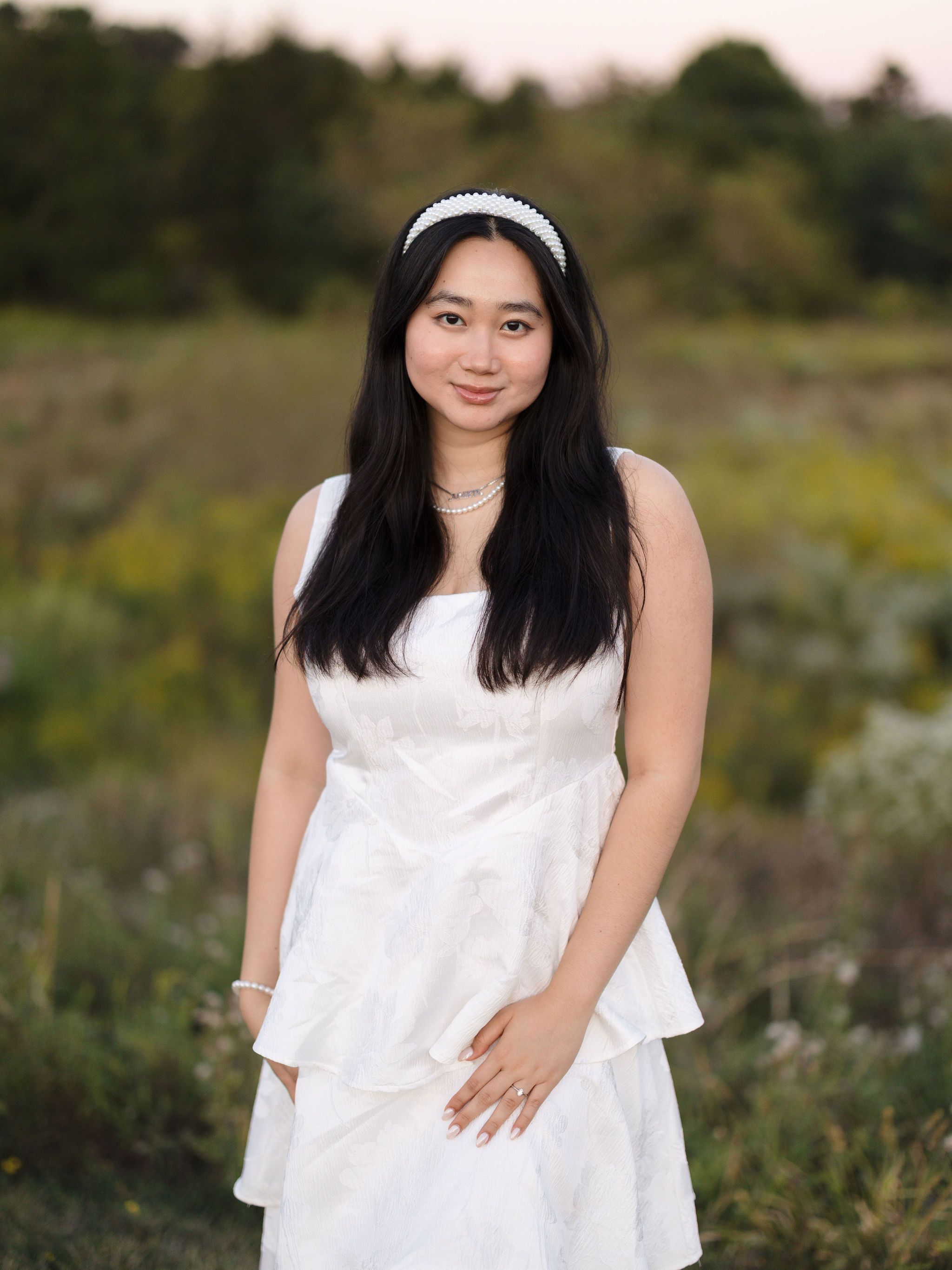A figure in a flowing white dress poses gracefully against a natural outdoor backdrop in golden sunlight.
