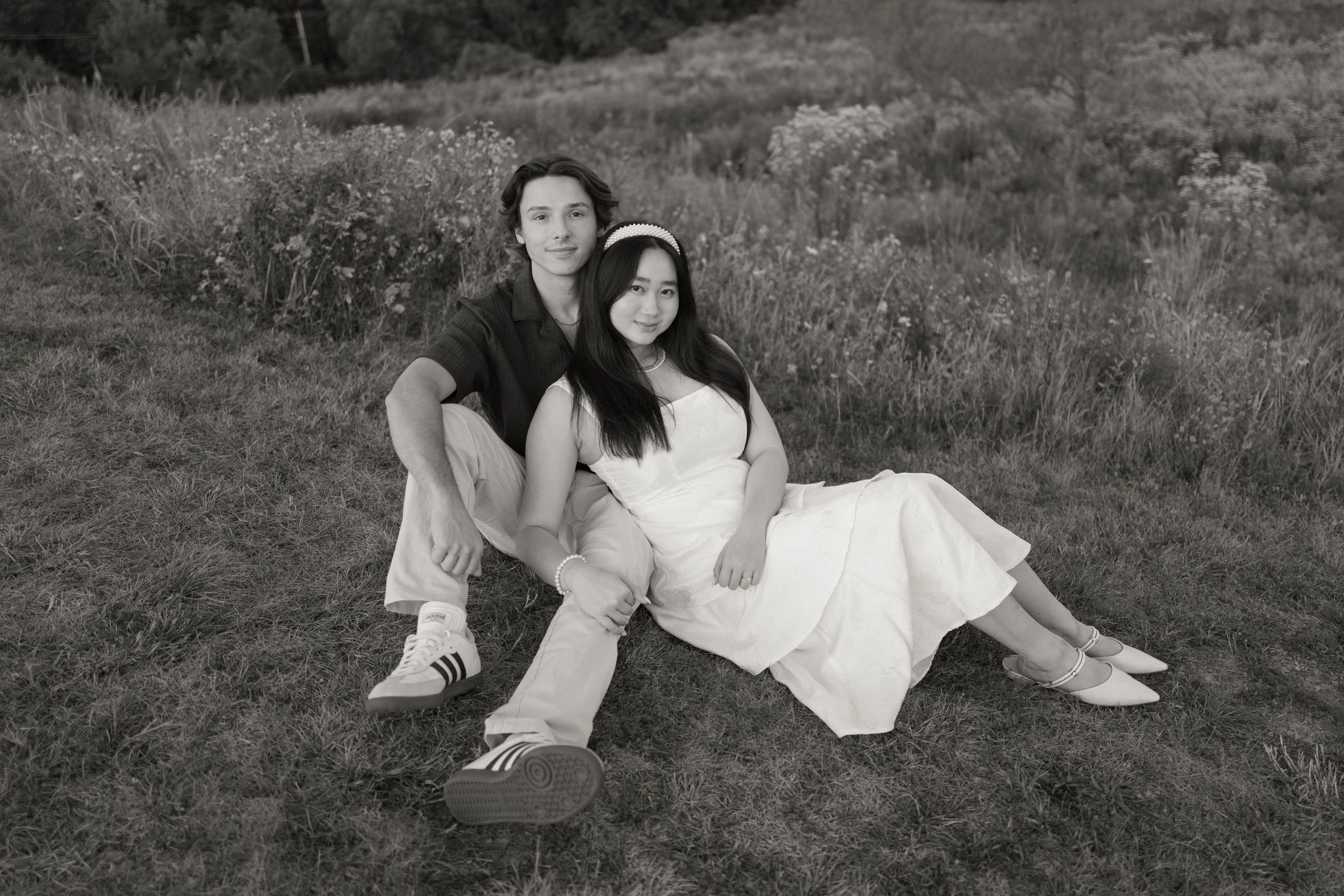 A black and white portrait of a couple sitting together in a grassy field.