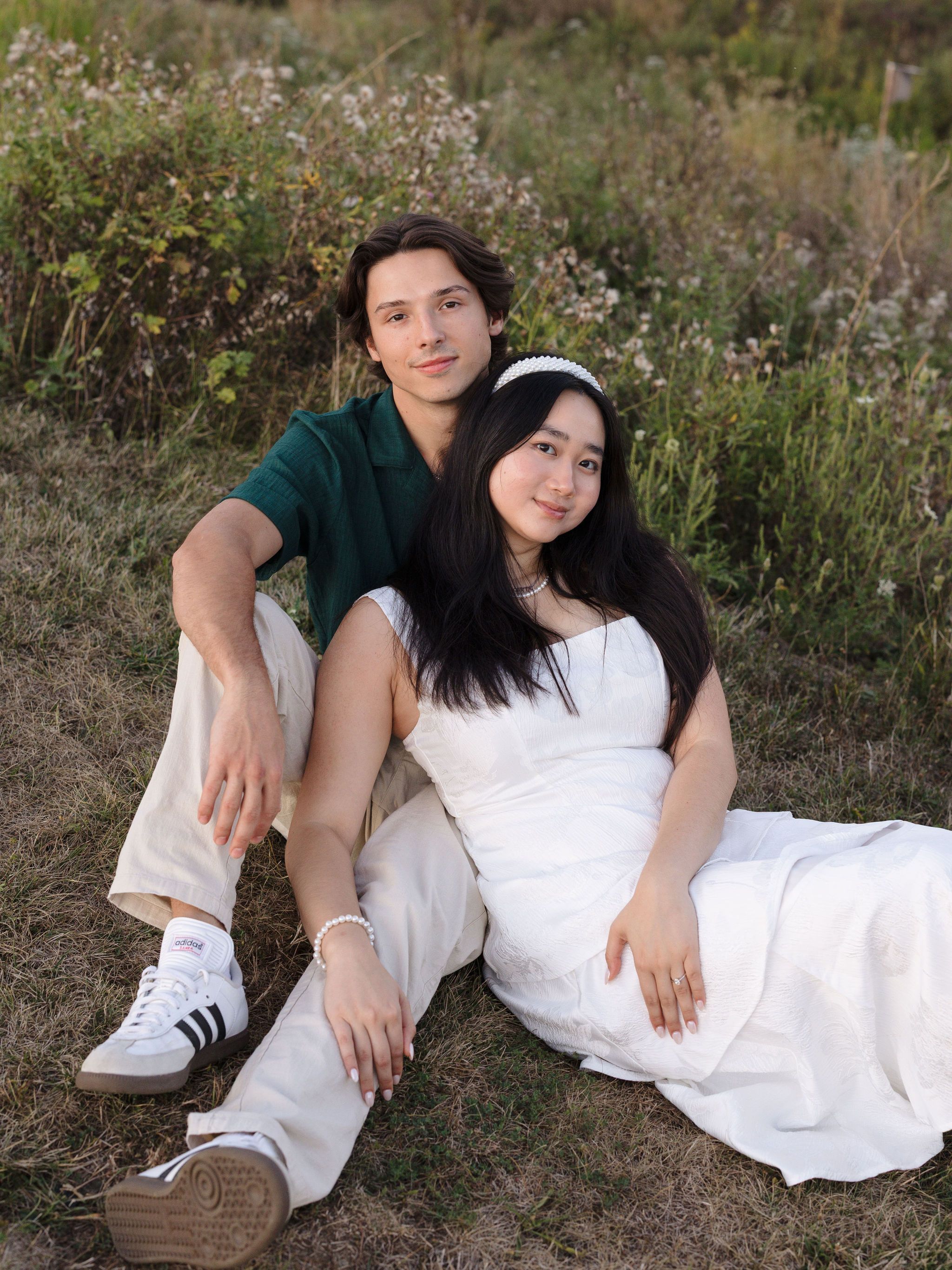 A couple relaxes together in a field of wildflowers wearing coordinated white and green outfits.