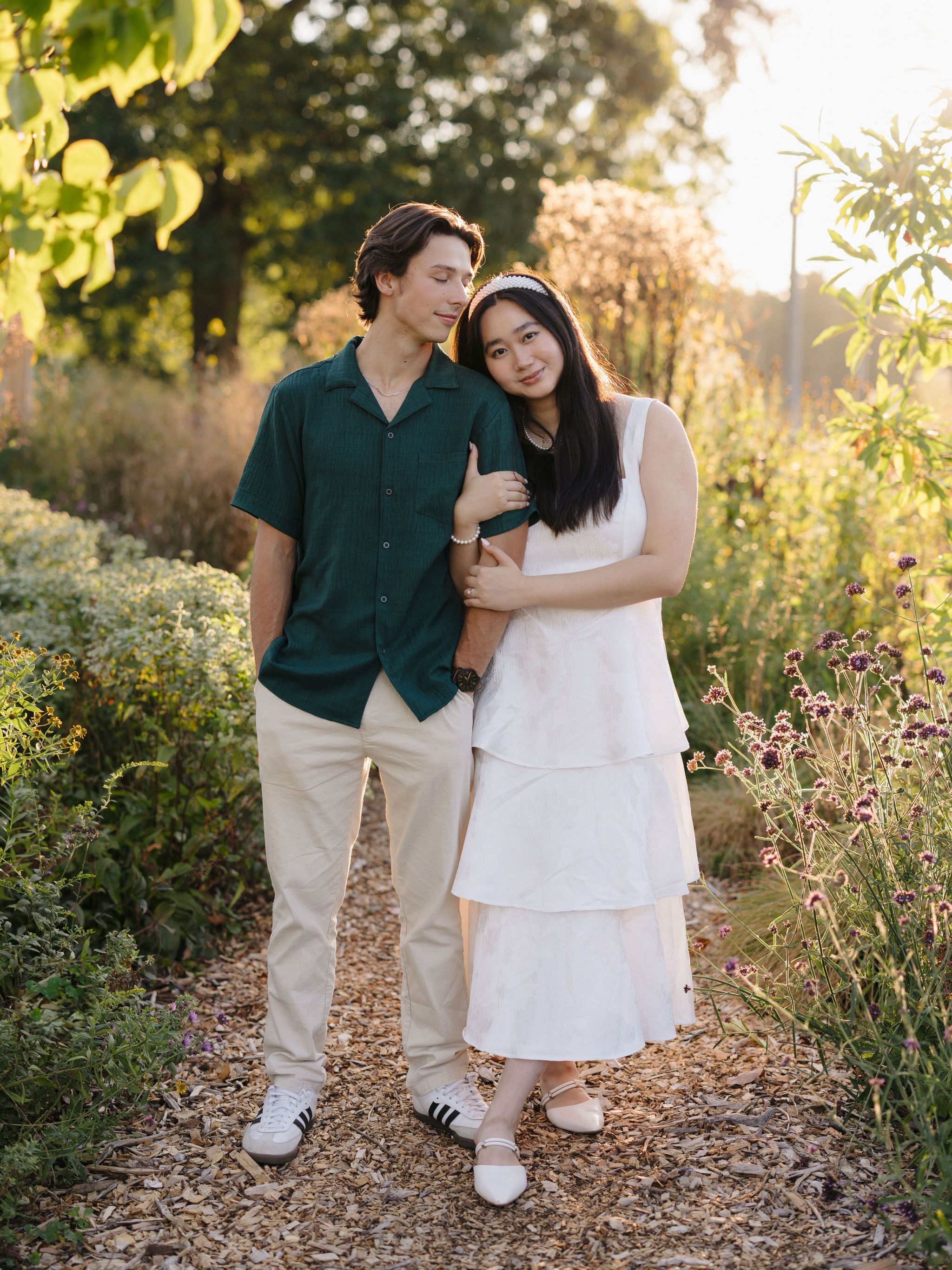 A romantic couple in casual attire shares an intimate moment in a garden setting during golden hour.