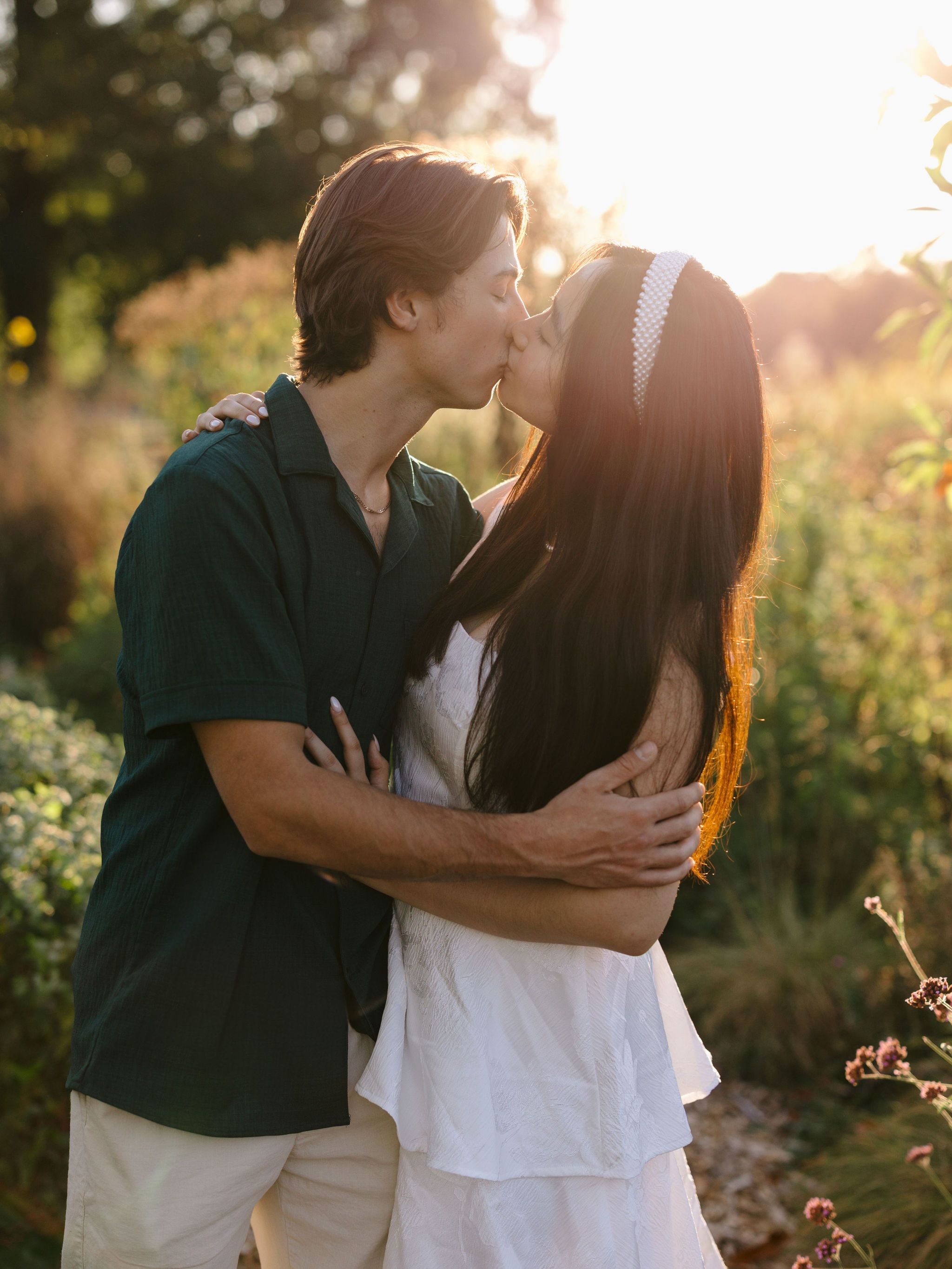 Couple sharing tender moments in a sunlit garden with backlit golden light filtering through trees.
