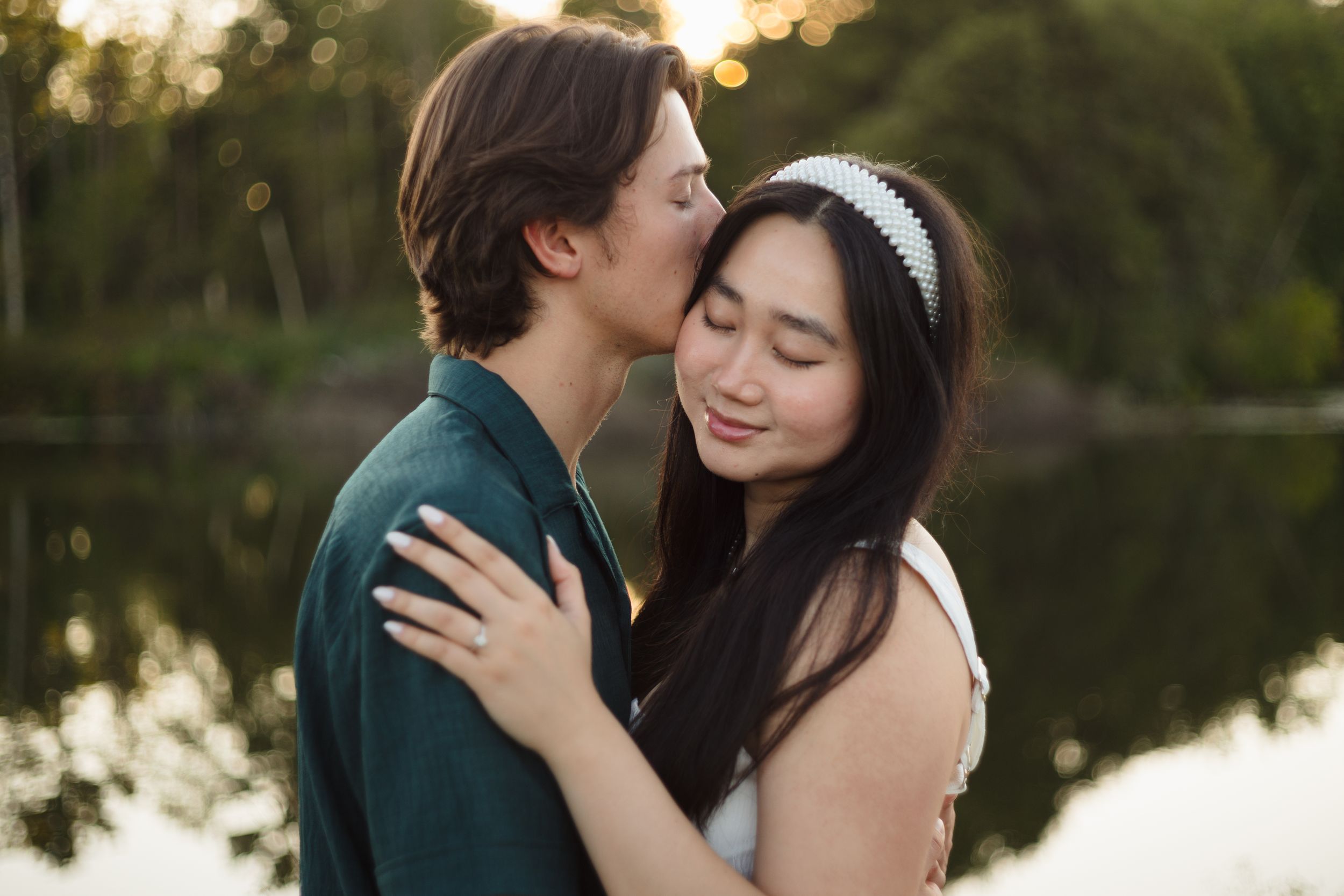 A couple shares intimate moments during a sunset photo session by a lake in a romantic outdoor setting.