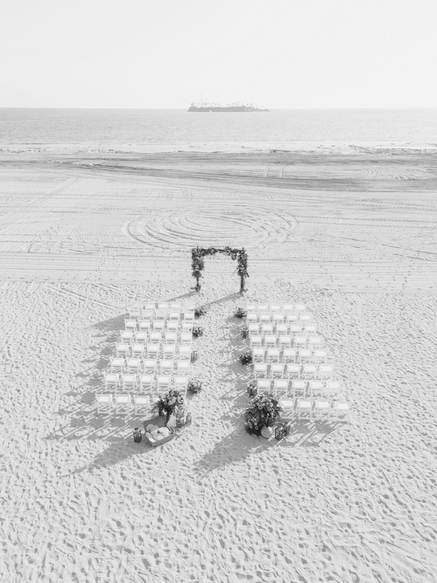 An aerial view of white chairs arranged on a snowy beach with an elegant floral arch for a winter wedding ceremony.