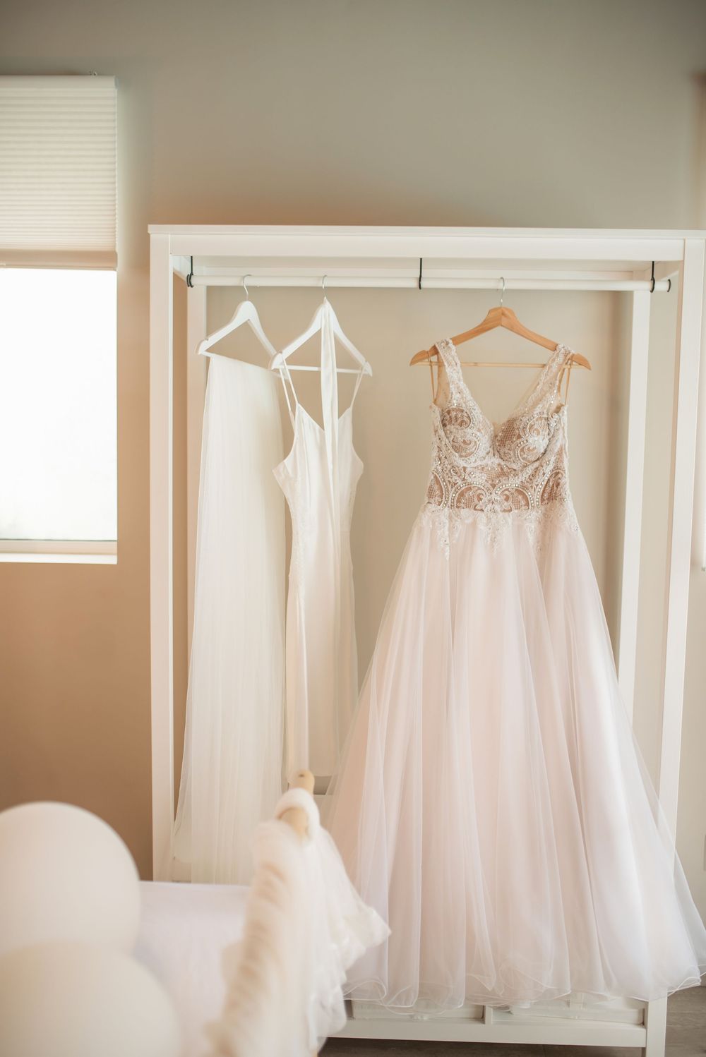 White and blush wedding dresses hanging on display in a well-lit dressing room.