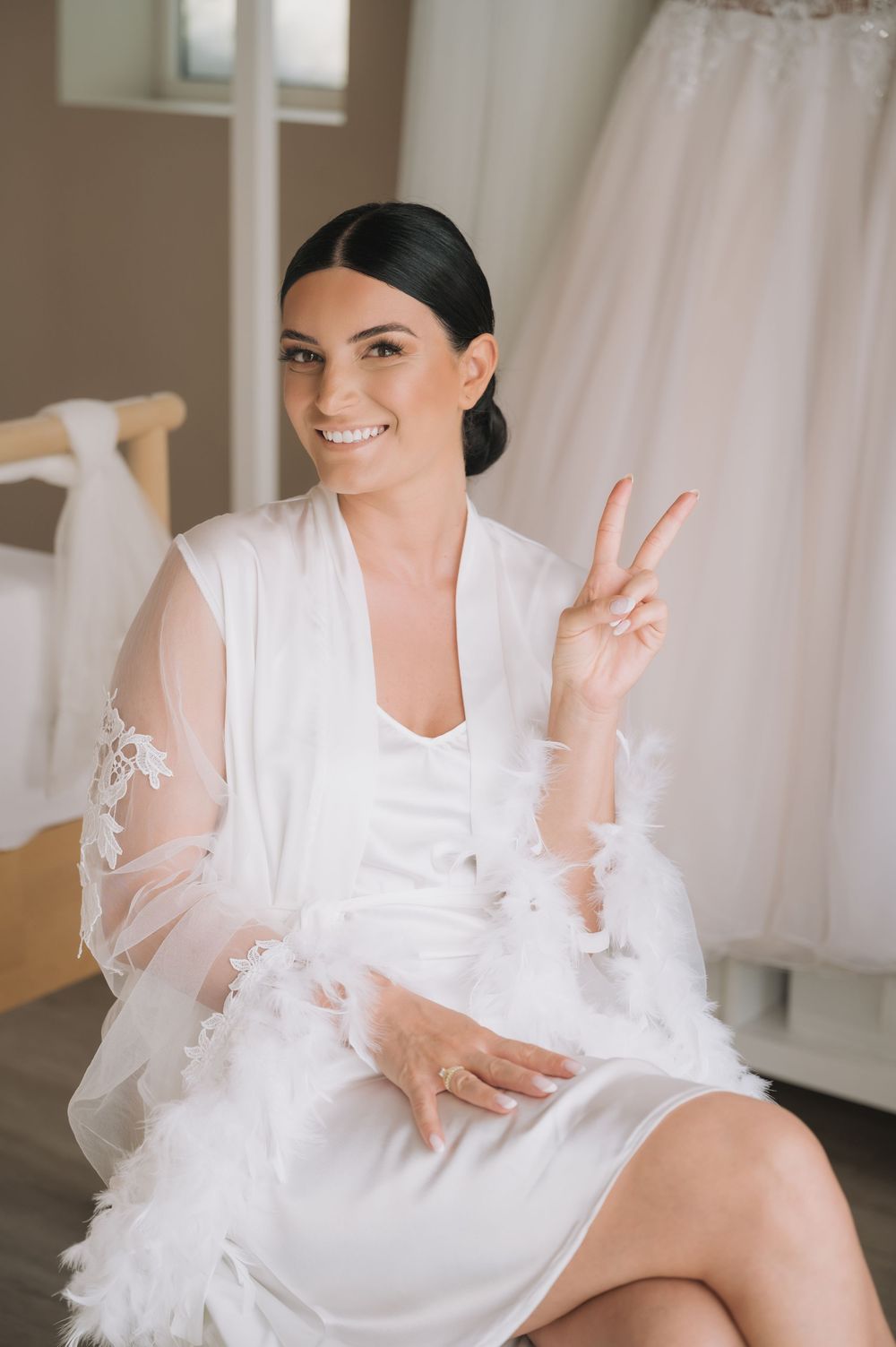 Woman in white bridal robe making playful poses in bright indoor setting.