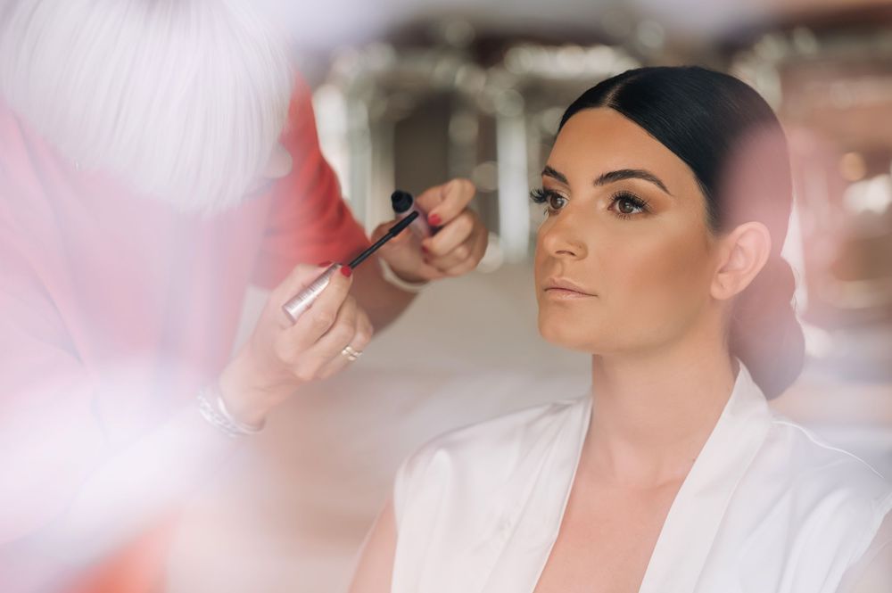 Woman in white getting professional makeup applied during bridal preparations.