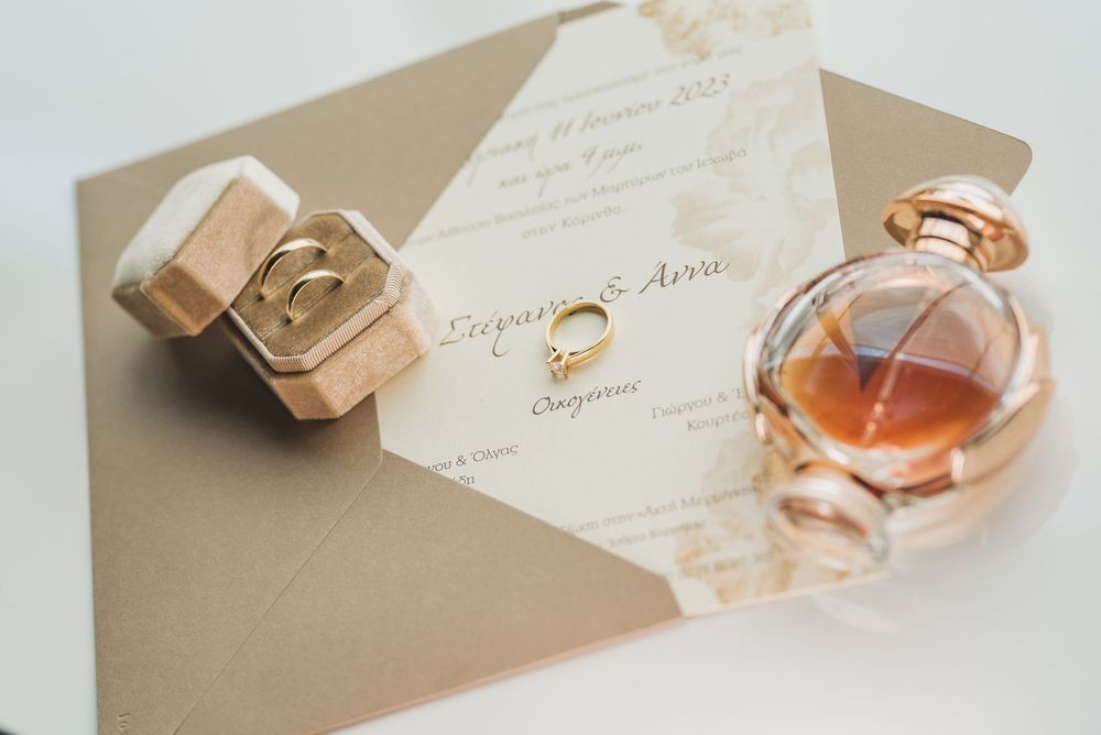 Wedding invitations and perfume bottles arranged on beige surface in natural light.
