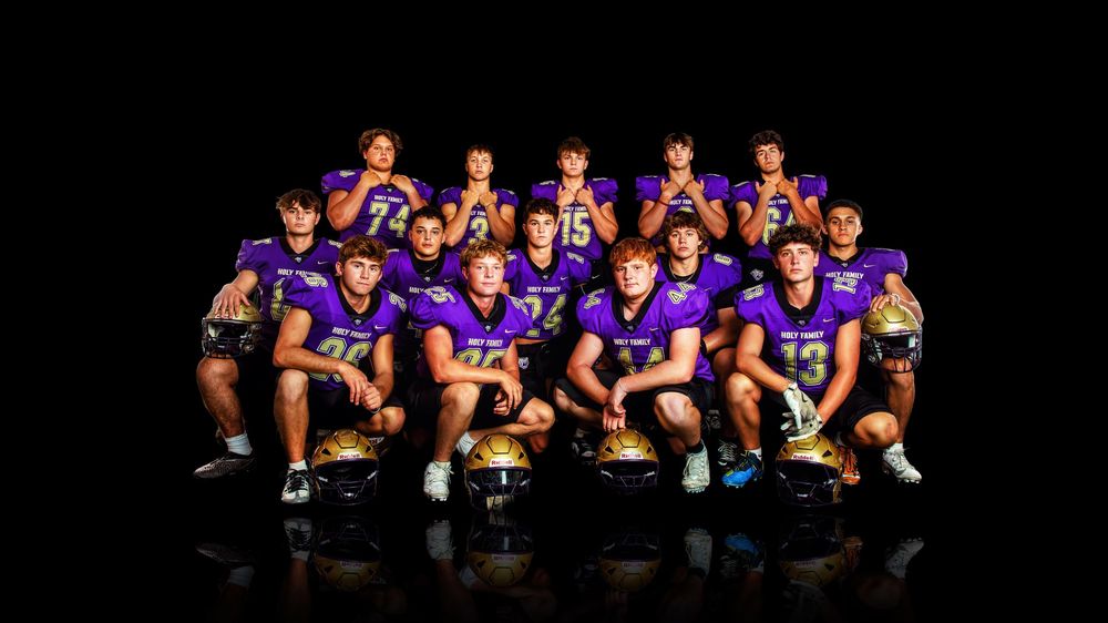 A group of athletes in purple jerseys pose together on bleachers for a team sports photo.