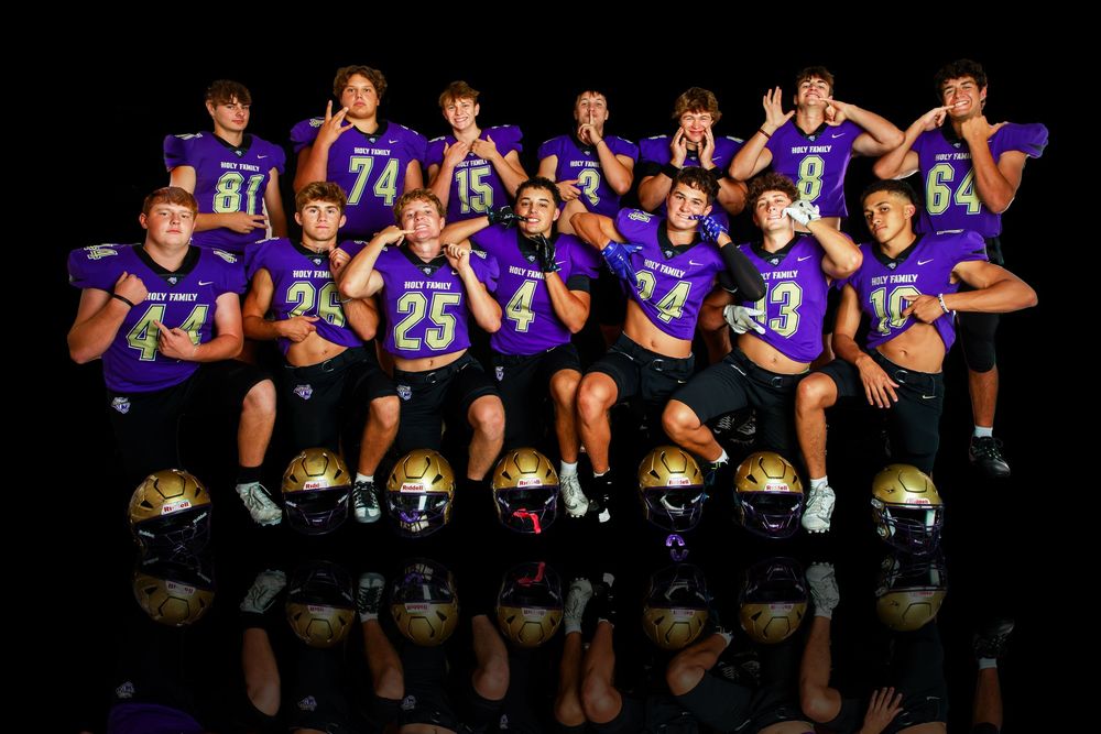 Football team sits in two rows wearing purple uniforms with reflective floor effect.
