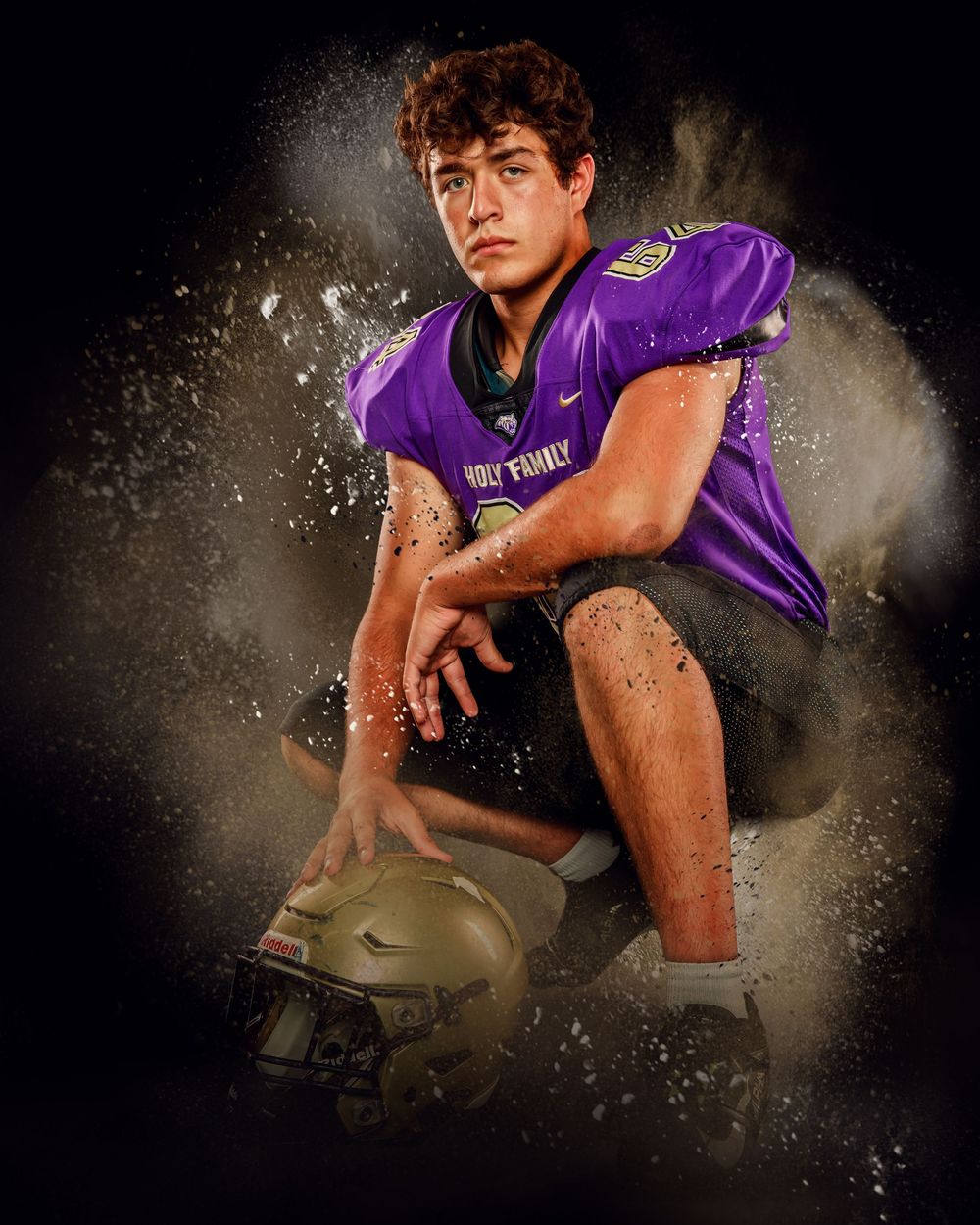 Dramatic sports portrait with dust effects of a player in purple uniform holding a gold helmet.