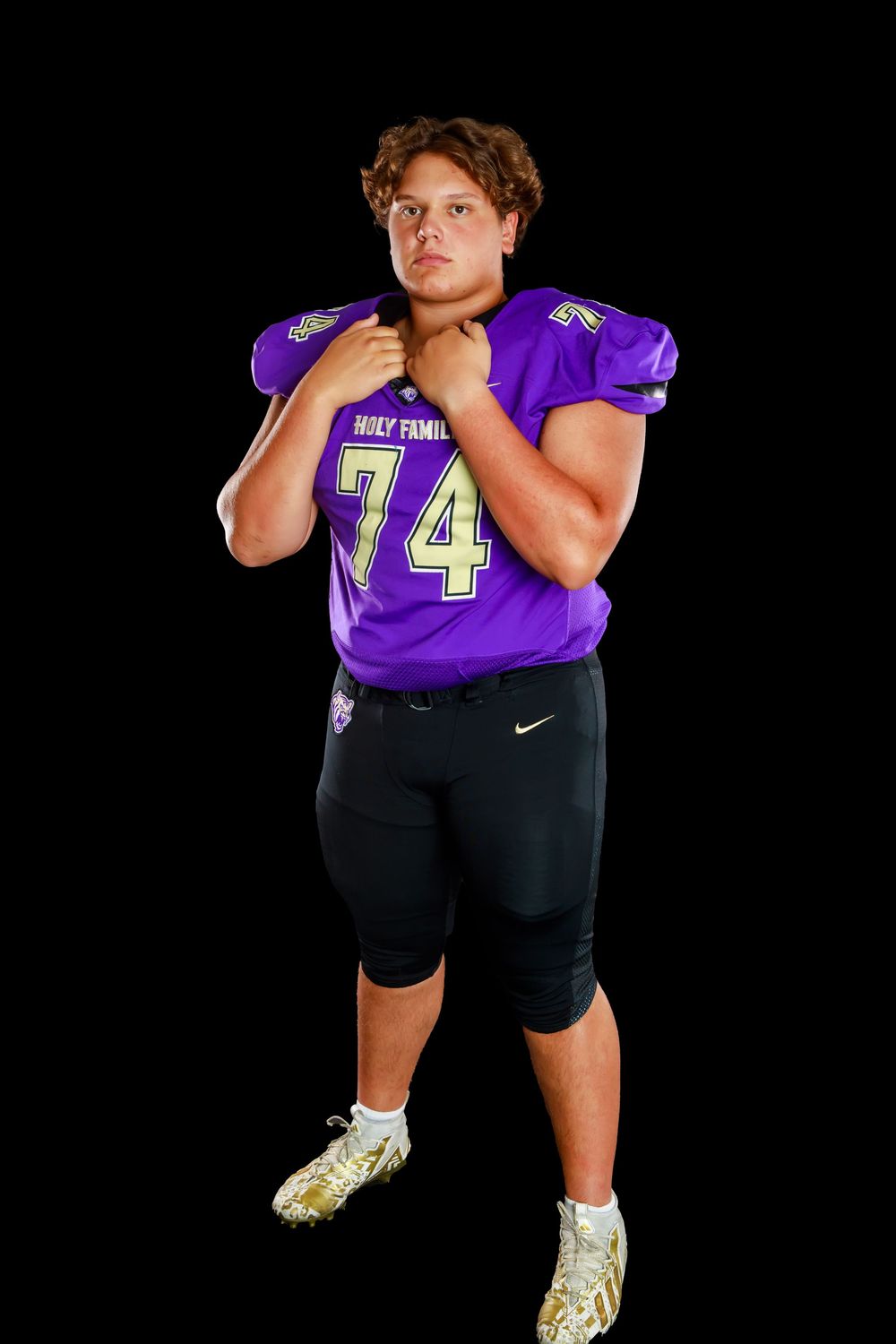 Football player wearing purple jersey number 74 poses in athletic stance against black background.