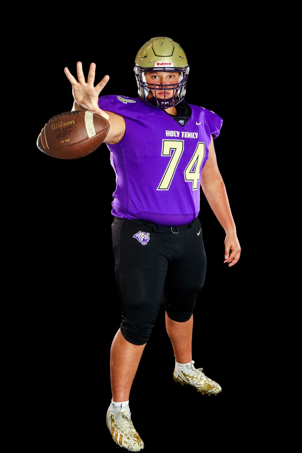 High school athlete in purple uniform holds football and extends hand in dynamic pose.
