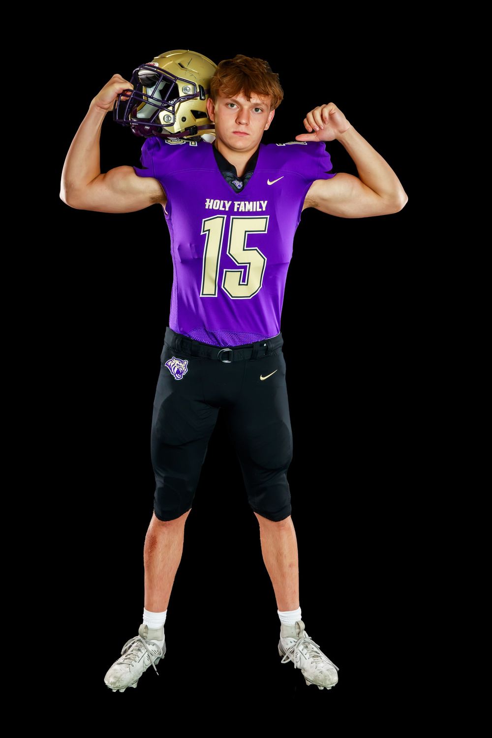 Football player in purple Holy Family jersey #15 flexes muscles while holding helmet against dark backdrop.
