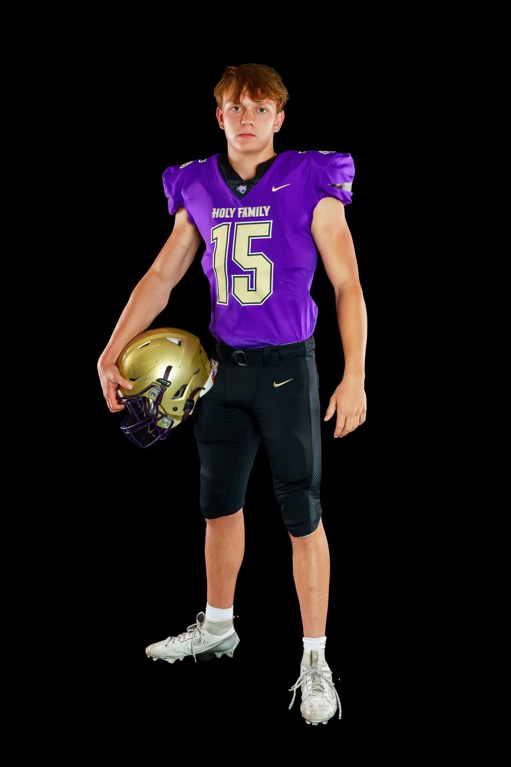 Football player in purple Holy Family jersey and black shorts holds gold football against black background.