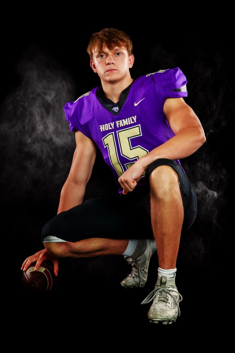 High school athlete in purple Holy Family uniform poses dramatically in low light studio setting.