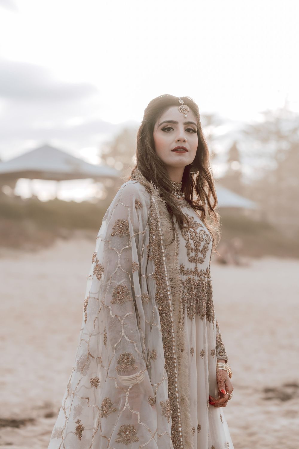 An ethereal beach photoshoot featuring someone in a delicate cream-colored lace ensemble against a soft, dreamy backdrop.